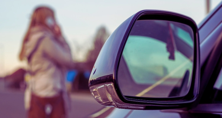 4 Mistakes to Avoid after a Rideshare Accident 6 A car side mirror and a worried woman using her smart phone.